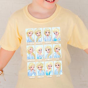 A yellow t-shirt with a collage of twelve different expressions of the Disney character Elsa, each accompanied by a word that describes the emotion.