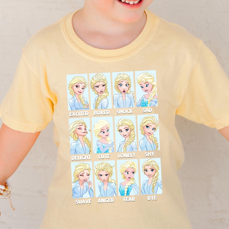 A yellow t-shirt with a collage of twelve different expressions of the Disney character Elsa, each accompanied by a word that describes the emotion.