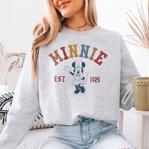 a woman sitting on a couch wearing a minnie mouse sweatshirt
