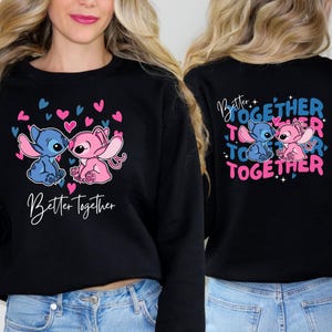 A woman wearing a black sweatshirt with a graphic design featuring two cartoon characters, one pink and one blue, along with the text "Better together" and hearts.