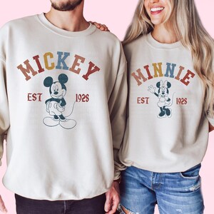 a man and a woman wearing mickey mouse sweatshirts