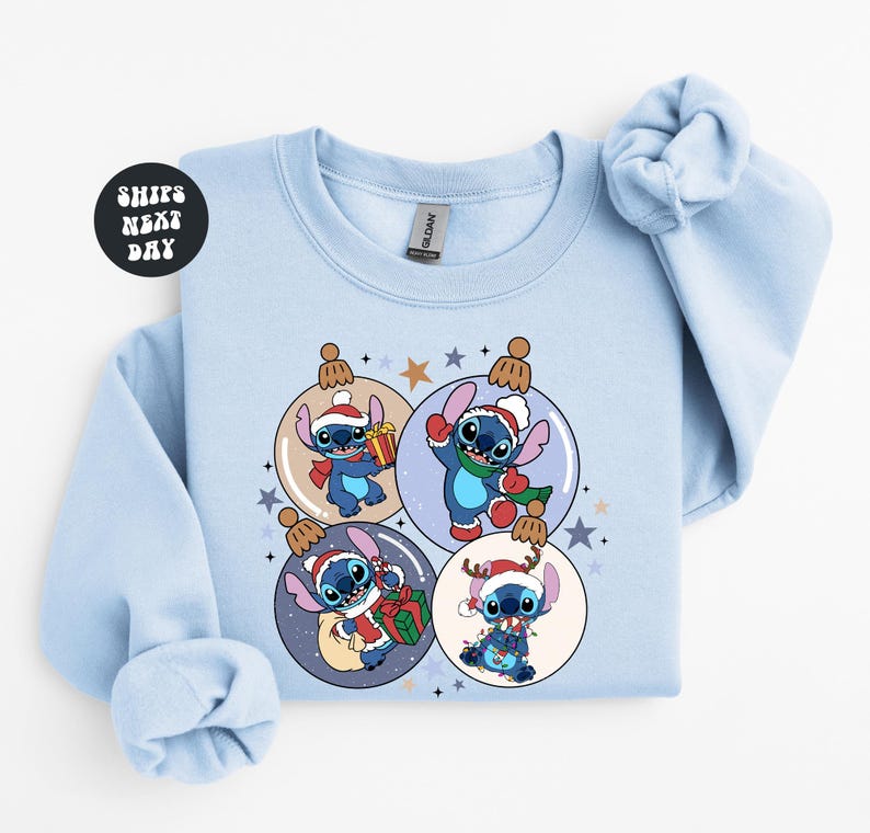 A light blue sweatshirt with a Christmas-themed design featuring four cartoon characters from the Lilo & Stitch movie franchise, each wearing a unique outfit and surrounded by festive ornaments.