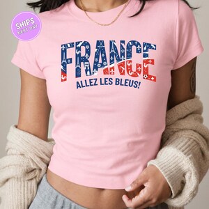 A woman wearing a pink t-shirt with the text "FRANCE ALLEZ LES BLUES!" printed on it.