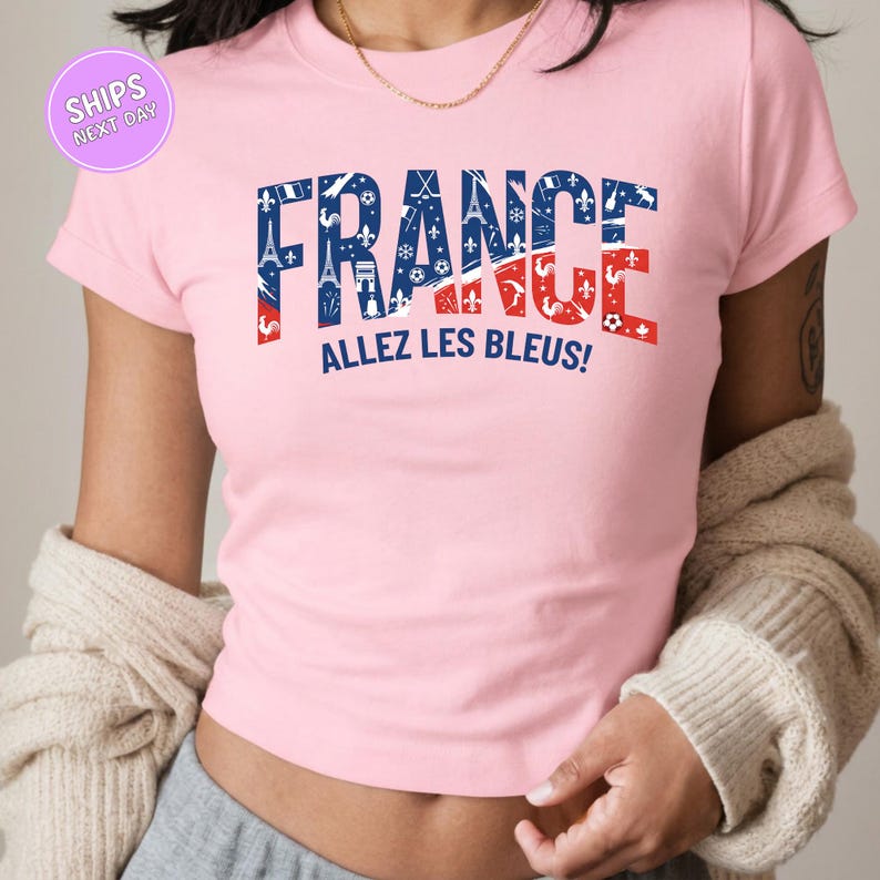 A woman wearing a pink t-shirt with the text "FRANCE ALLEZ LES BLUES!" printed on it.
