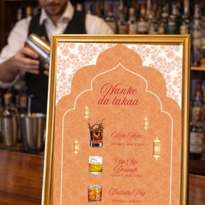 Puede incluir: Un letrero enmarcado en oro con un fondo melocotón y un diseño floral muestra un menú de bebidas. El letrero dice "Nanke da takaa" y enumera cócteles: Vata Vola, Sip Sip Dosanjh y Patiala Peg. El fondo es de color melocotón.
