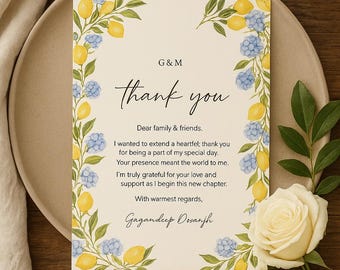 May include: A thank you card with floral and lemon accents. The card features the text "thank you" in elegant script, with a message below. The card is surrounded by yellow lemons and blue flowers. Two white roses are in the foreground.