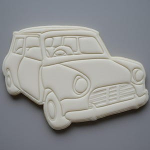 May include: A white car-shaped cookie cutter with detailed features, including windows, wheels, and a front grill. The design is a classic car style, perfect for baking themed treats. The cutter is made of a light-colored material.