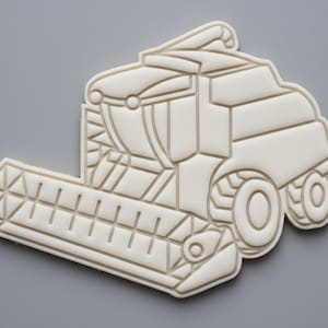 Puede incluir: Cortador de galletas beige con forma de cosechadora. El cortador presenta un diseño detallado de la máquina agrícola, que incluye ruedas, cabina y cabezal de cosecha. El cortador está hecho de plástico y es adecuado para hacer galletas o decoraciones de fondant.