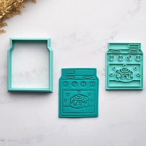 Könnte beinhalten: Drei türkisfarbene Ausstecher: ein Glas und zwei Ofenformen. Die Ofenausstecher zeigen ein Zimtschnecken-Design mit Herzen. Der Glasausstecher hat eine einfache rechteckige Form. Ideal zum Backen von Keksen.
