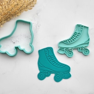 May include: Three teal roller skate cookie cutters. One is a simple outline, and the other two are detailed with laces and wheels. The cutters are made of plastic and are designed for baking. The image is shot from above.