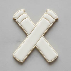 Puede incluir: Una galleta blanca en forma de X con un diseño decorativo. La galleta está hecha de una masa de color claro y está decorada con glaseado blanco. El diseño presenta una serie de líneas curvas en la parte superior de cada brazo de la X.