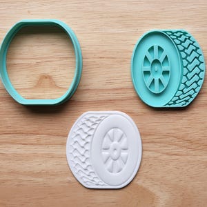May include: Three cookie cutters in the shape of a tire. One is a teal colored oval, the second is a teal tire shape, and the third is a white tire shape. The tire shapes have detailed tread patterns.
