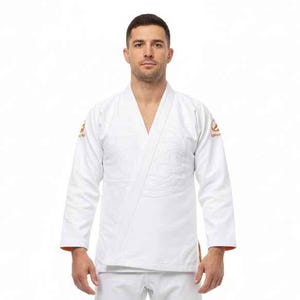 May include: White martial arts uniform with a wrap-style top and matching trousers. The uniform has orange accents on the shoulders and cuffs. The person is standing in front of a white background.