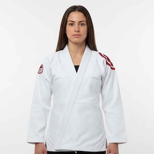 Könnte beinhalten: Ein weißer Kampfsportanzug mit roten Akzenten auf den Schultern und einem Logo auf dem linken Ärmel. Der Anzug hat einen V-Ausschnitt. Der Hintergrund ist weiß.
