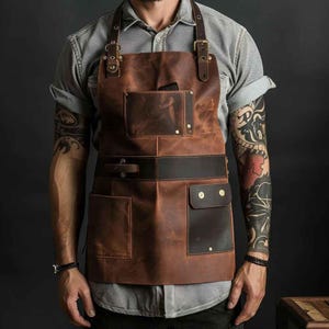 May include: A brown leather apron with multiple pockets and adjustable straps. The apron has a dark brown belt and pocket accents, with brass-coloured rivets and buckles. The apron is designed for use in a kitchen or workshop.