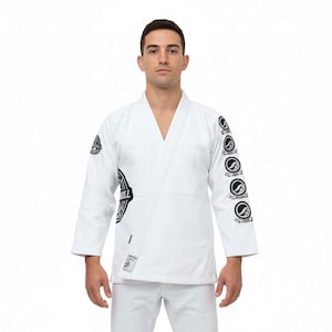 May include: White martial arts uniform with black logos. The jacket has a V-neck and logos on the sleeves and chest. The trousers are white. The uniform is designed for martial arts training and competition.