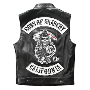 May include: Black leather vest with the words "SONS OF ANARCHY" and "CALIFORNIA" in white lettering. A patch featuring a grim reaper with a scythe and a machine gun is centered on the back. The vest has a classic biker style.