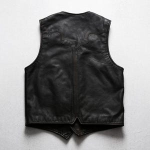 May include: A black leather vest with a classic design. The vest has a V-neck and a decorative stitched pattern on the upper back. The leather appears to be slightly distressed, giving it a vintage look.