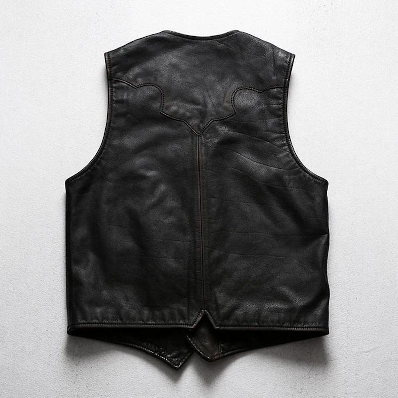 May include: A black leather vest with a classic design. The vest has a V-neck and a decorative stitched pattern on the upper back. The leather appears to be slightly distressed, giving it a vintage look.