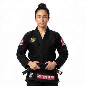 May include: Black Jiu-Jitsu uniform with a black belt. The uniform has patches on the sleeves and chest. The belt is tied around the waist. The brand name "SHOYOROLL" is visible on the uniform.
