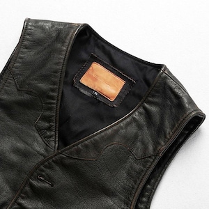 May include: Close-up of a black leather vest with a V-neck design. The vest has a button closure and decorative stitching along the edges. A brown leather label is sewn inside the vest. The vest is XL size.