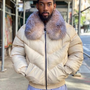 Könnte beinhalten: Cremefarbene Steppjacke mit Pelzkragen und schwarzem Reißverschluss. Die Jacke hat ein gestepptes Design und zwei Vordertaschen. Das Model trägt eine graue Jogginghose. Ein Winter-Oberbekleidungsartikel.