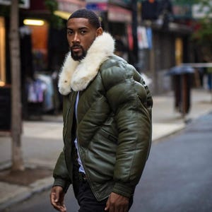 May include: Olive green puffer jacket with a cream-colored faux fur collar. The jacket has a quilted design and ribbed cuffs. The person is wearing a white shirt and black pants. The background is a city street.