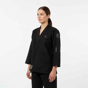 May include: Black martial arts uniform, comprising a V-neck jacket and trousers. The jacket has a logo on the chest and sleeve, with the word "WAZAR" printed on the sleeve. This uniform is designed for martial arts training and competition.