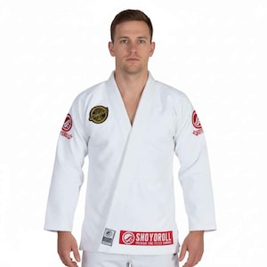 May include: White martial arts uniform with long sleeves and a V-neck. The uniform features red and gold patches with the text "SHOYOROLL" and other logos. The uniform is designed for martial arts training and competition.