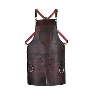 May include: A dark brown leather apron with a cross-back design. The apron features two large pockets, metal rivets, and a chest pocket. The straps are a burgundy color and the apron has two metal rings.