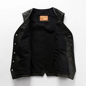 May include: Black leather vest with a button-up front and a black interior lining. The vest has a classic design with a small, rectangular patch inside the back. A stylish outerwear piece.
