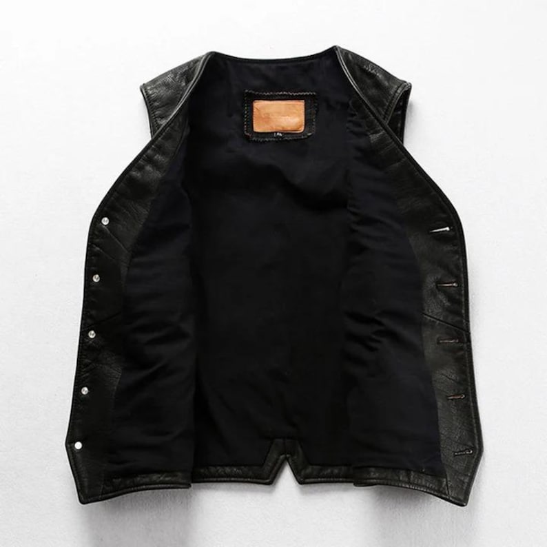 May include: Black leather vest with a button-up front and a black interior lining. The vest has a classic design with a small, rectangular patch inside the back. A stylish outerwear piece.