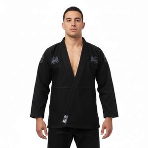 Puede incluir: Uniforme negro de artes marciales con cuello en V. El uniforme presenta escudos de león bordados en los hombros y un pequeño parche cerca de la cintura. La parte superior de manga larga y los pantalones están hechos de tela duradera.