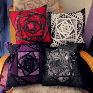 Może przedstawiać: Cztery dekoracyjne poduszki z geometrycznym wzorem róży. Poduszki są w różnych kolorach, w tym czerwonym, czarnym, białym i fioletowym. Poduszki są ułożone na krześle z tkaniną w kwiatowy wzór.