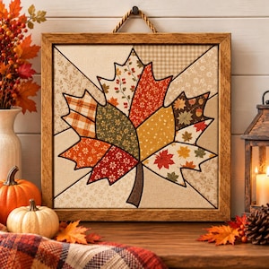 May include: A square wall art piece featuring a central maple leaf design composed of various fabric patches in autumn colors including orange, red, yellow, and green, enclosed in a textured brown wooden frame with a rope hanger.