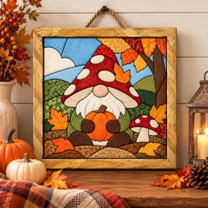 May include: A square framed fabric wall hanging featuring a gnome with a red mushroom-patterned hat holding an orange pumpkin. The scene includes a blue sky, green hills, brown tree trunks, and scattered orange and yellow autumn leaves.