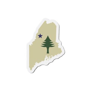 May include: A sticker in the shape of the state of Maine, with a tan background. A dark green pine tree and a dark blue star are featured on the sticker. The sticker has a white border.