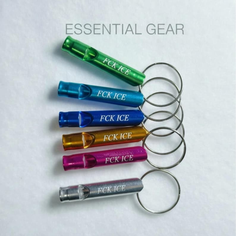 May include: An assortment of six metal whistles in various colors, including green, blue, gold, purple, and silver, each attached to a silver keyring. The text "FCK ICE" is printed on each whistle. The words "ESSENTIAL GEAR" are printed above the whistles.