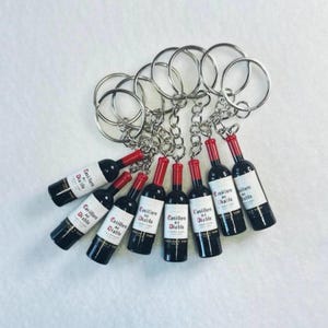 May include: A collection of keychains featuring miniature wine bottle charms. The black bottles have red tops and white labels with the text "Casillero del Diablo". Each keychain has a silver chain and a large silver ring.