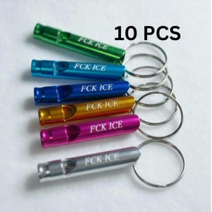 May include: An assortment of six metal whistles in various colors, including green, blue, gold, pink, and silver. Each whistle is attached to a silver key ring and has the text "FCK ICE" printed on it. The image also displays the text "10 PCS".