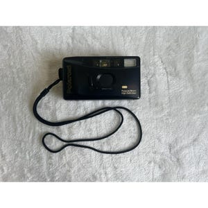 May include: Black Polaroid 35mm High Definition camera with a black strap. The camera has a flash and a lens. The word "Polaroid" is printed in gold on the camera.