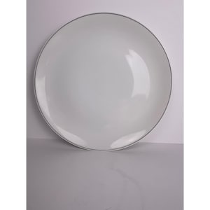 Op de afbeelding: Een witte keramische plaat met een dunne grijze rand. De plaat is rond en heeft een licht hol midden. De plaat staat tegen een witte achtergrond.