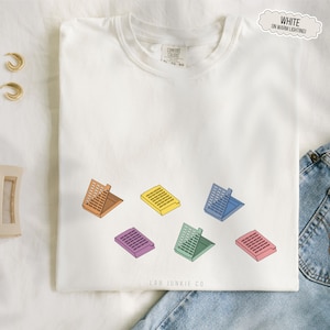 May include: White t-shirt with a crew neck featuring a colorful graphic of six open, rectangular containers in shades of orange, yellow, blue, purple, green, and pink. The text "LAB JUNKIE CO" is printed at the bottom.