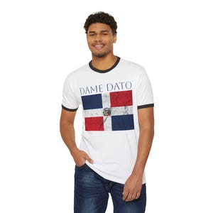 May include: White ringer t-shirt with black trim featuring the Dominican Republic flag and the text "DAME DATO" in blue. The flag design includes blue and red squares with the Dominican Republic coat of arms in the center.