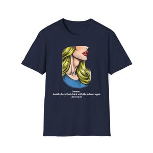 May include: Navy blue t-shirt featuring a pop art style illustration of a woman's face with blonde hair and red lips. The text on the shirt reads "Ummm... doublecheck that chick with the adam's apple just sayin'".