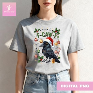 Könnte beinhalten: Graues T-Shirt mit einem festlichen Design, das eine schwarze Krähe mit Weihnachtsmütze, Weihnachtsschmuck und dem Text "F-CAW-F" zeigt. Das Design umfasst Stechpalme, eine Zuckerstange und einen Stern. Der Text "DIGITAL PNG" steht unten.