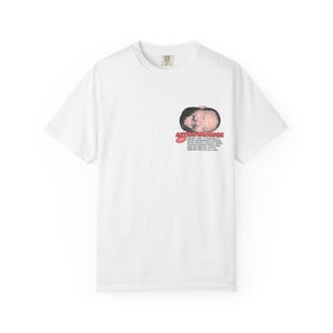 Puede incluir: Camiseta blanca con un gráfico de la cara de un hombre y el texto "ACTION BRONSON" en rojo. Texto adicional impreso debajo de la cara. La camiseta tiene cuello redondo y mangas cortas.