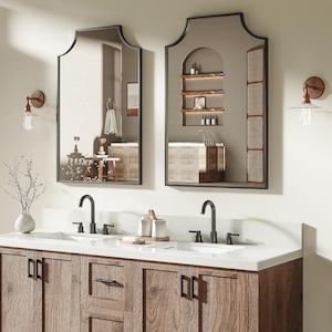 May include: A double vanity with a white countertop and two sinks. The wooden cabinet has a natural finish and black hardware. Two arched mirrors hang above the sinks, along with sconce lighting. The vanity has a lower shelf for storage.