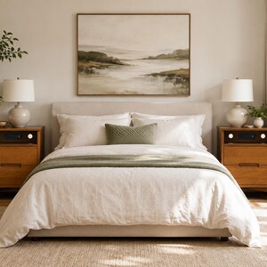 May include: A bedroom set featuring a beige upholstered bed frame with white bedding, a green throw blanket, and a green lumbar pillow. Two wooden nightstands with built-in speakers and white lamps flank the bed, with a landscape painting above.