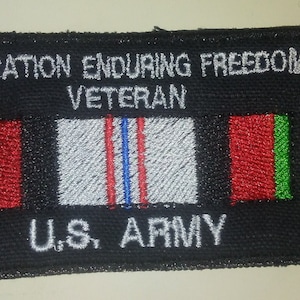 May include: Black patch with white text "Operation Enduring Freedom Veteran U.S. Army". The patch features a white ribbon with red and blue stripes and two green and red flags.